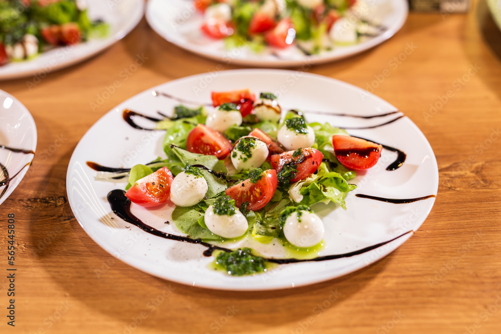 Plate of healthy classic close-up caprese salad with mozzarella cheese tomatoes and basil in kitchen - italian cuisine