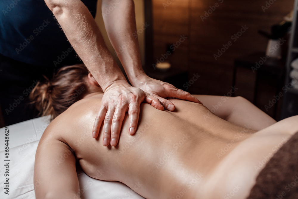 Fototapeta premium Male masseur doing back massage to client woman in dark room of massage spa