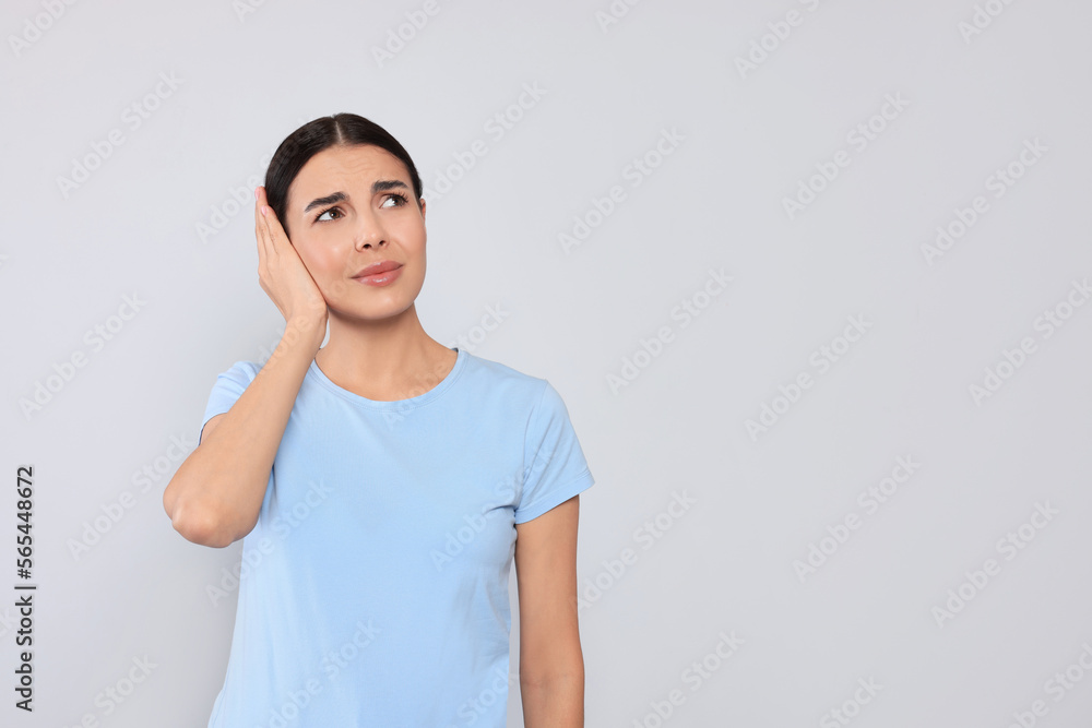 Young woman suffering from ear pain on light grey background. Space for text