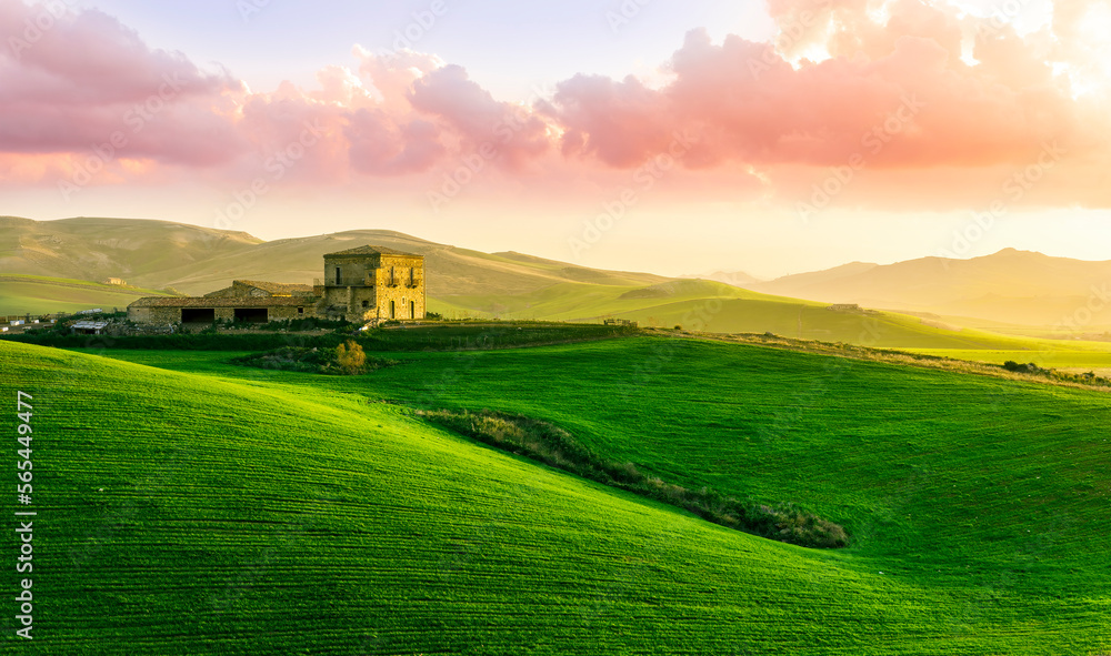 countryside sunset in green hills of spring fields with old castle farm and mountains on background of evening landscape