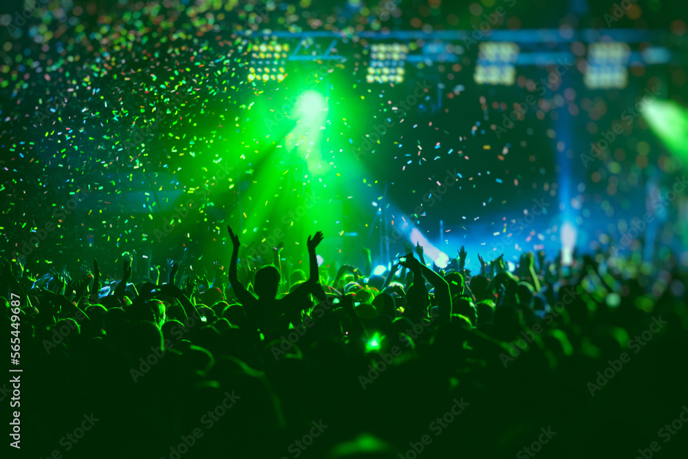 A crowded concert hall with scene stage green lights, rock show performance, with people silhouette, colourful confetti explosion fired on dance floor air during a concert festival