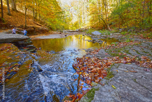 As fall reflects in McCormick's Creek, one hiker assists another as they make their way upstream, Indiana.