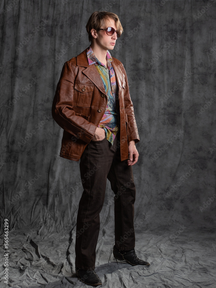 confident dude in a colorful shirt and brown leather jacket, a portrait in sunglasses in the studio on a gray background