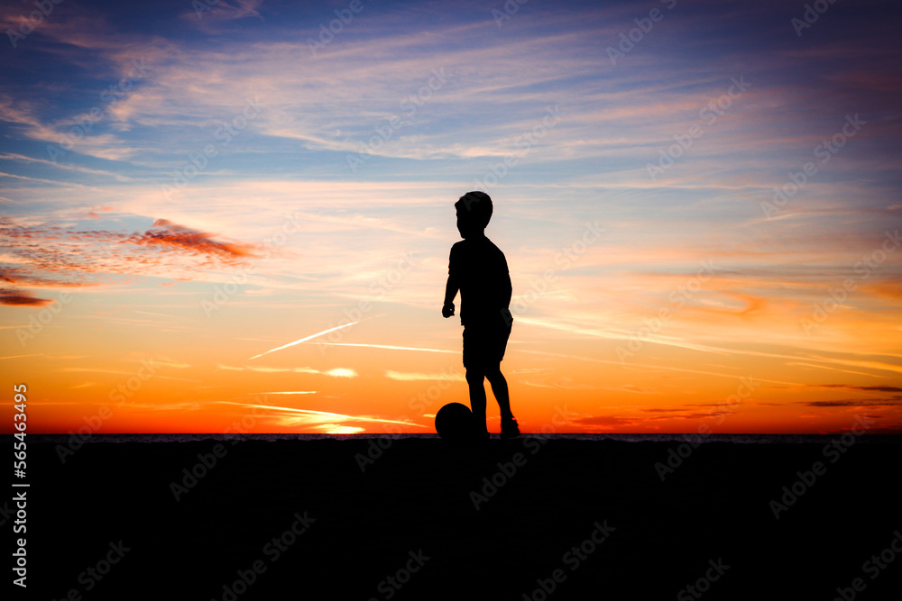 silhouette of boy playing soccer at sunset on beach