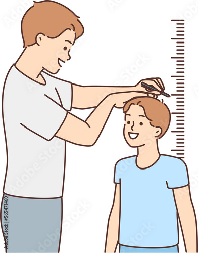 Smiling father measure son height near wall