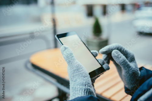 Mobile phone with blank white screen in female hands in gloves