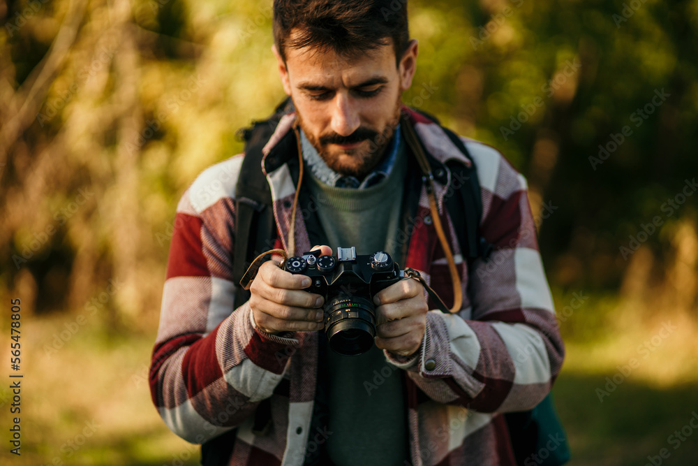 Hipster photographer checking photos and enjoying photo shooting camera on wild nature sunset. Hobby blog leisure concept