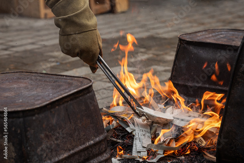Western Raku reduction bins being loaded with ceramic pottery using heat resistant gloves and tongs into a fire made with newspaper strips