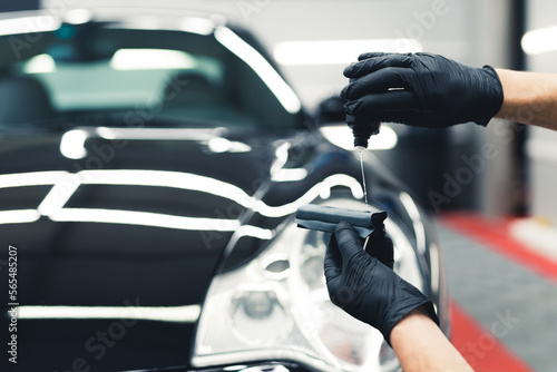 Close-up shot man hands wearing black gloves applying ceramic coating liquid to sponge to use on car. Car detailing process. Horizontal indoor shot. High quality photo