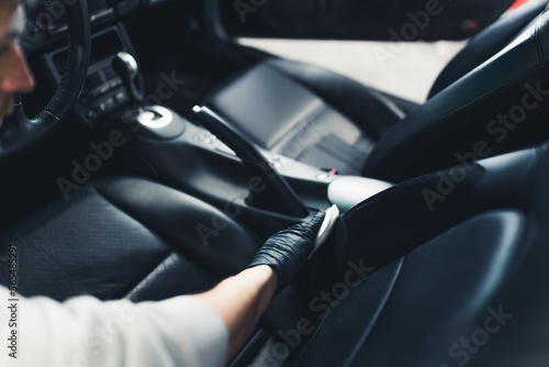 Unrecognisable man wearing black gloves putting protective coating on leather car seats. Waterproofing car upholstery. Car detailing process. Horizontal indoor shot. High quality photo