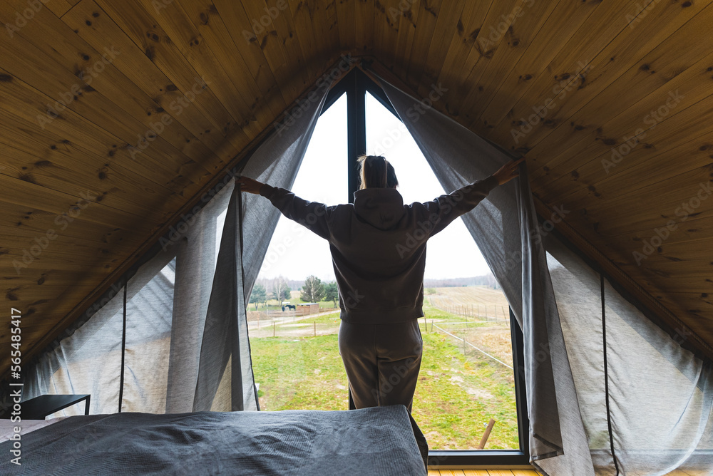 A woman dressed in gray enters an attic room. The ceiling is wooden. The woman opens the curtains. High quality photo A woman dressed in gray enters an attic room. The ceiling is wooden. The woman opens the curtains. High quality photo