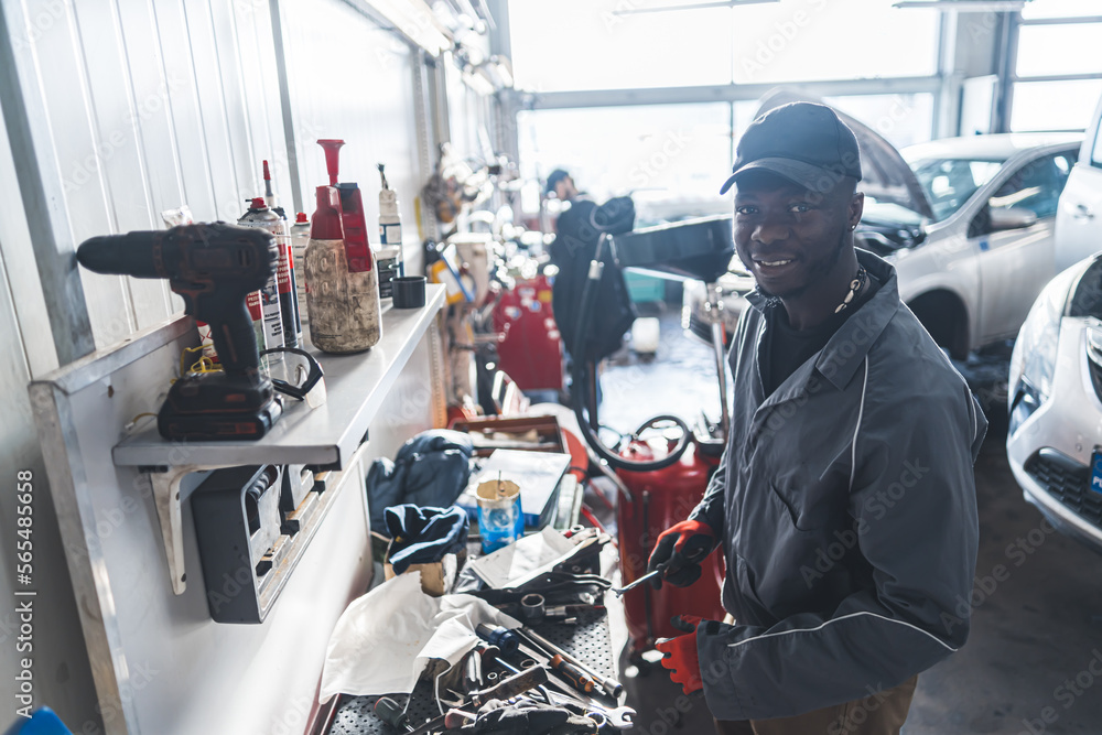 Shot of a repair shop with a black mechanic standing by a workbench in the foreground and a white mechanic working in the background. High quality photo