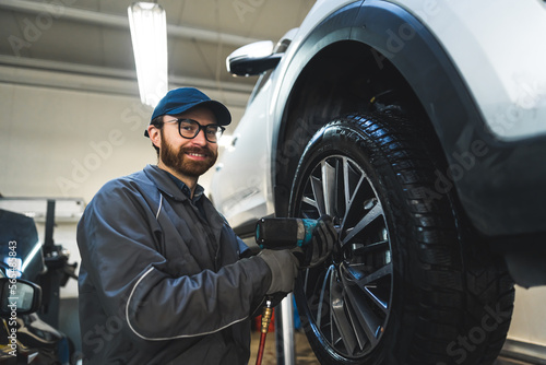 Low-angle shot of a smiling mechnic screwing a car wheel. Repair shop concept. High quality photo