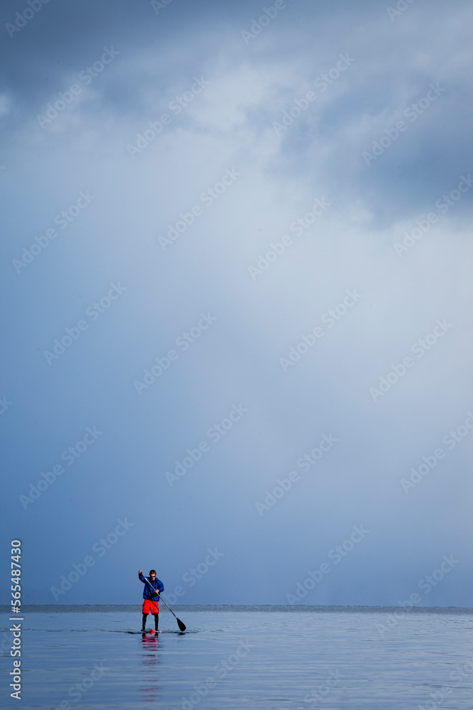One man standup paddleboarding on a mountain lake in winter with a storm approaching. One man standup paddleboarding on a mountain lake in winter with a storm approaching.