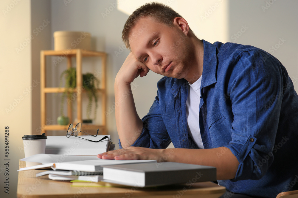 Tired man studying at wooden table indoors Tired man studying at wooden table indoors