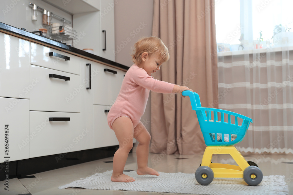 Cute baby with toy walker in kitchen near window. Learning to walk