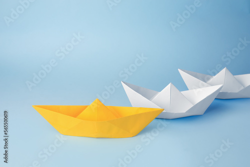 Group of paper boats following yellow one on light blue background. Leadership concept