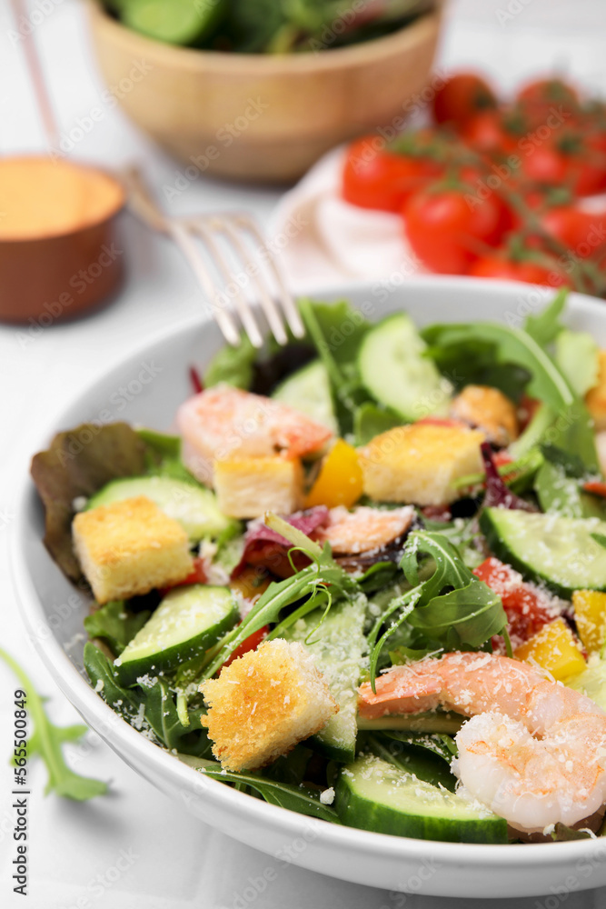Delicious salad with croutons, cucumber and shrimp served on white tiled table, closeup Delicious salad with croutons, cucumber and shrimp served on white tiled table, closeup