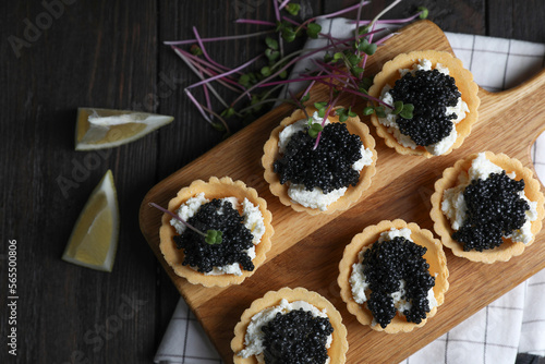 Board of delicious tartlets with black caviar and cream cheese on wooden table, top view