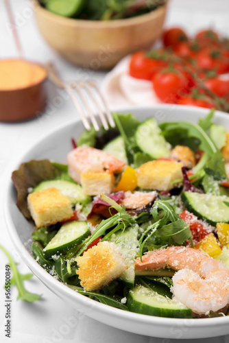 Delicious salad with croutons, cucumber and shrimp served on white tiled table, closeup