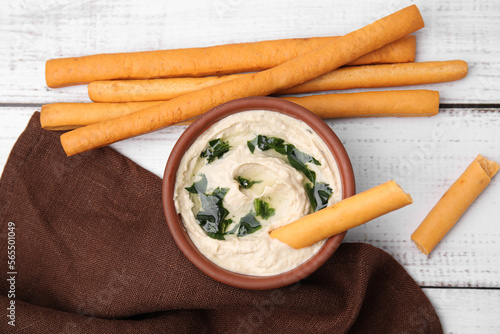 Delicious hummus with grissini sticks on white wooden table, flat lay