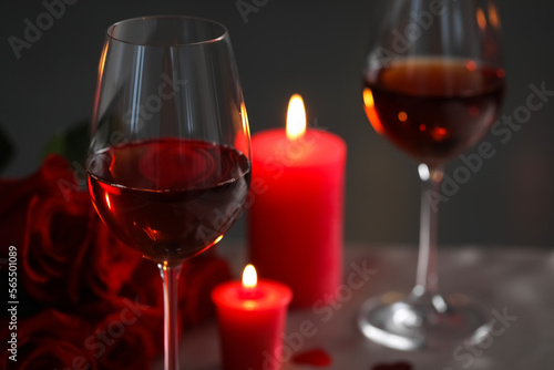 Romantic table setting with glasses of red wine, burning candles and rose flowers against blurred background