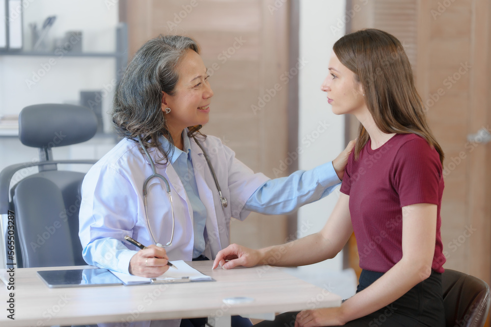 Fototapeta premium Female elder doctor takes a history of a patient and gives a consultation about osteopathy to a female patient after measuring blood pressure and heart rate and encouragement by holding hands