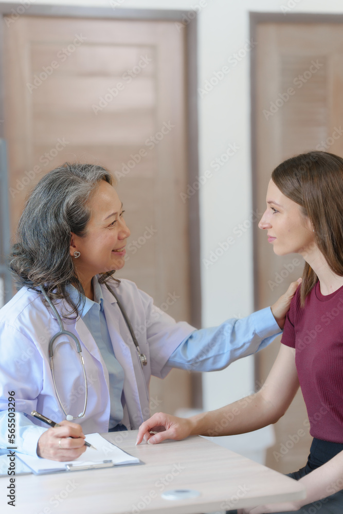 Female elder doctor takes a history of a patient and gives a consultation about osteopathy to a female patient after measuring blood pressure and heart rate and encouragement by holding hands Female elder doctor takes a history of a patient and gives a consultation about osteopathy to a female patient after measuring blood pressure and heart rate and encouragement by holding hands