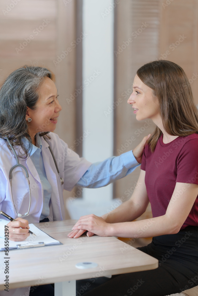 Female elder doctor takes a history of a patient and gives a consultation about osteopathy to a female patient after measuring blood pressure and heart rate and encouragement by holding hands Female elder doctor takes a history of a patient and gives a consultation about osteopathy to a female patient after measuring blood pressure and heart rate and encouragement by holding hands