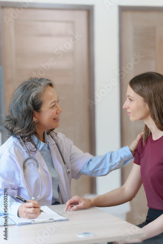 Female elder doctor takes a history of a patient and gives a consultation about osteopathy to a female patient after measuring blood pressure and heart rate and encouragement by holding hands