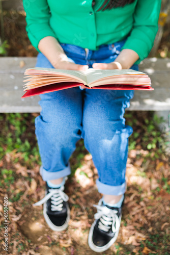 Unrecognizable girl with a green blouse and jeans, reading a book in the backyard with the sunlight. World book day