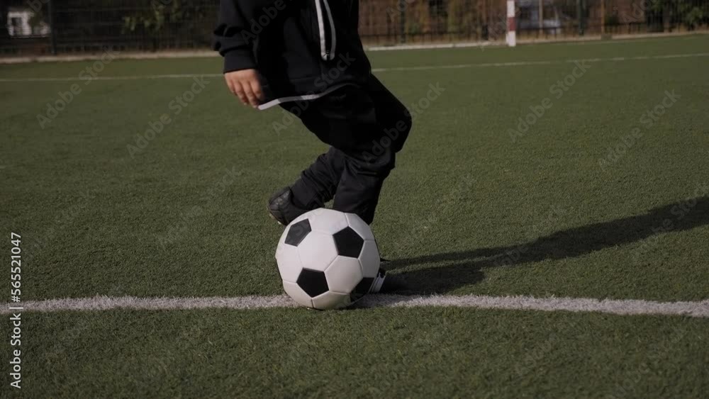 A little boy in a sports uniform trains on a football field with a ball, he jumps and puts his feet on the ball. Children's soccer training. A little boy in a sports uniform trains on a football field with a ball, he jumps and puts his feet on the ball. Children's soccer training.
