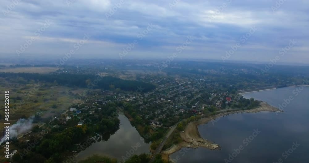 Scenery of a village locating on the bank of the river. Drone footage over the landscape on grey cloudy autumn day. Scenery of a village locating on the bank of the river. Drone footage over the landscape on grey cloudy autumn day.