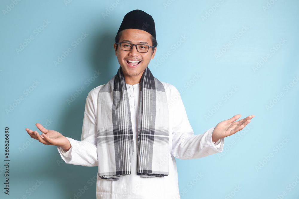 Portrait of Asian muslim man in white koko shirt with skullcap pulling hands towards camera, inviting someone to come inside, welcoming gesture. Isolated image on blue background Portrait of Asian muslim man in white koko shirt with skullcap pulling hands towards camera, inviting someone to come inside, welcoming gesture. Isolated image on blue background