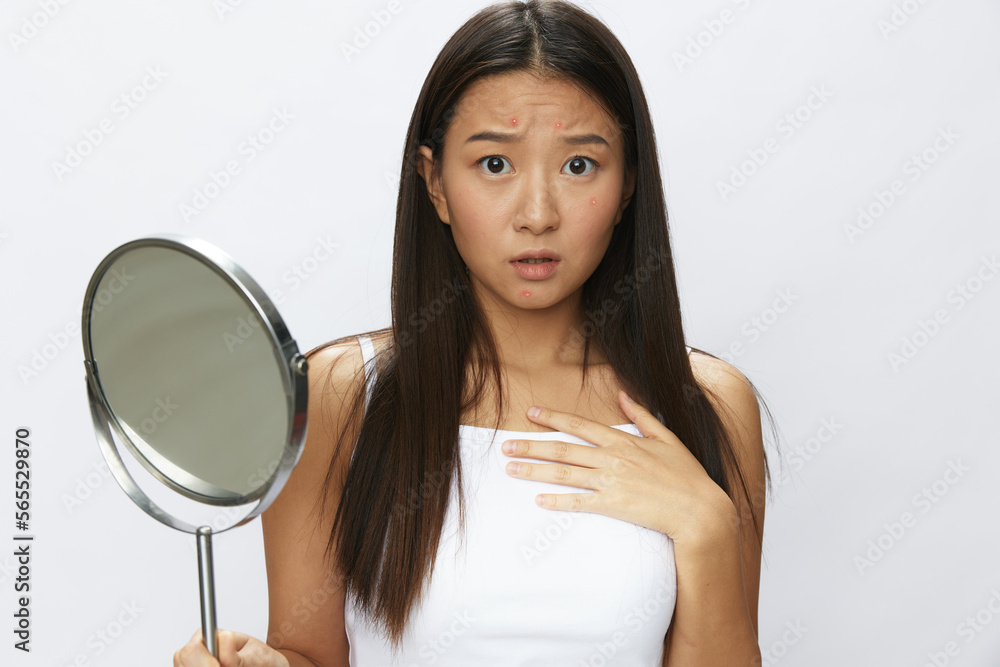 Asian woman with mirror in hand facial skin problems, acne and inflammation, red rash and allergies, chicken pox, sadness from rashes. Facial skin care concept for diseases and nerves Asian woman with mirror in hand facial skin problems, acne and inflammation, red rash and allergies, chicken pox, sadness from rashes. Facial skin care concept for diseases and nerves