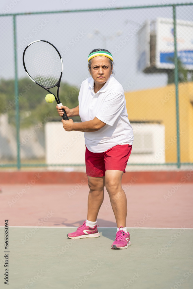 Active senior woman playing tennis on court.