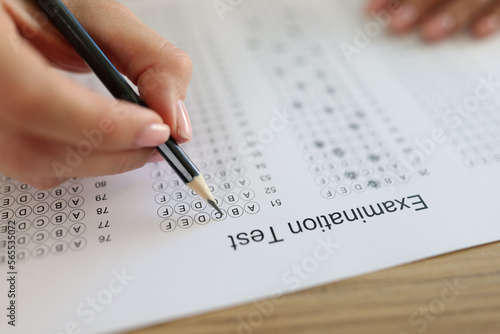 Student's hand holds pencil over paper with test questions.