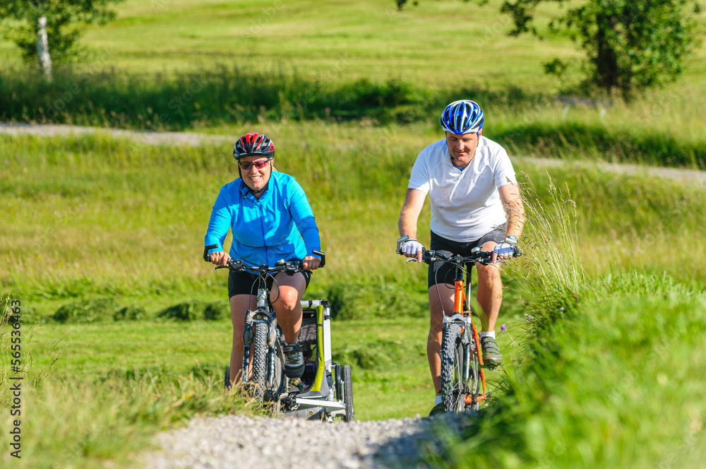 Raus ins Grüne mit dem Fahrrad - Eltern mit Nachwuchs im Buggy unterwegs mit dem Mountainbike Raus ins Grüne mit dem Fahrrad - Eltern mit Nachwuchs im Buggy unterwegs mit dem Mountainbike