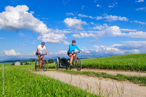 Eltern mit Nachwuchs im Buggy unterwegs mit dem Mountainbike, die Voralpen-Landschaft im Allgäu genießen 