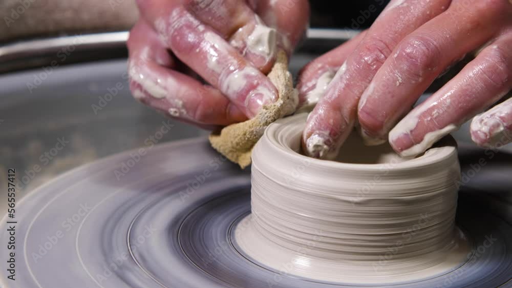 A potter works on a potter's wheel. The girl's hands use a sponge to mold a mug of clay in the workshop. Slow motion A potter works on a potter's wheel. The girl's hands use a sponge to mold a mug of clay in the workshop. Slow motion