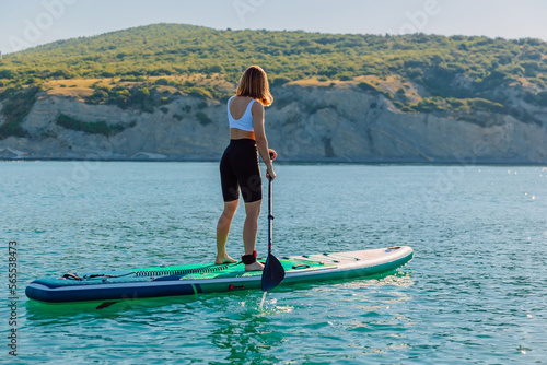 Young woman on stand up paddle board at quiet sea with beautiful landscape. © artifirsov