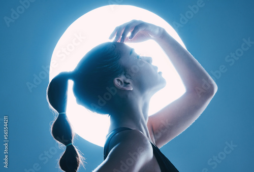 Beauty, light and profile of a model in a studio with a sensual, soft and attractive pose. Cosmetic, magical and slim woman with a mystical glow posing by a moon while isolated by a blue background. photo