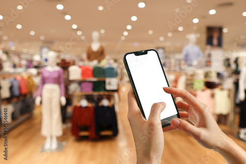Woman holding mobile phone pressing payment for online shopping against blurred background of department stores. Online shopping concepts.