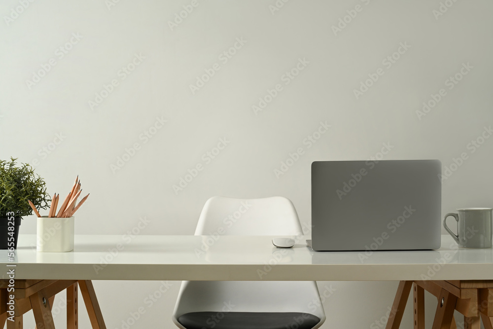 Obraz premium Modern home office interior with laptop computer, pencil holder, coffee cup and potted plant on white table