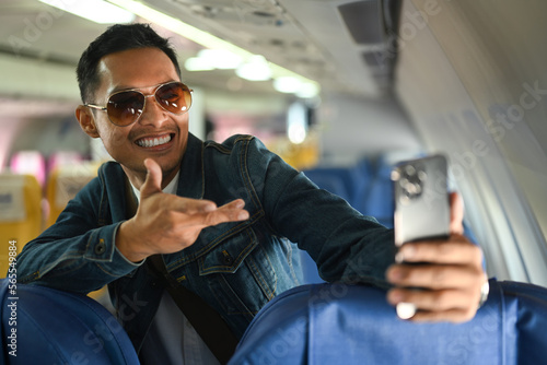 Playful male passengers waving hand, having video call on smart phone while standing in aircraft cabin