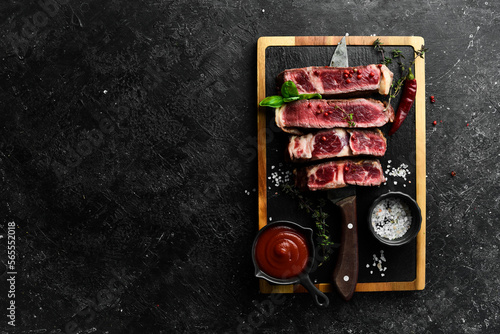 Steak on the bone on the kitchen board. Tomahawk steak on a black wooden background. Top view. Free space for copying.