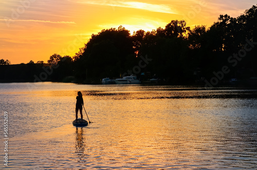 Girl paddling on SUP board on beautiful lake during sunset or sunrise, standing up paddle boarding morning adventure in Germany lake district Mecklenburg  © Iuliia Sokolovska