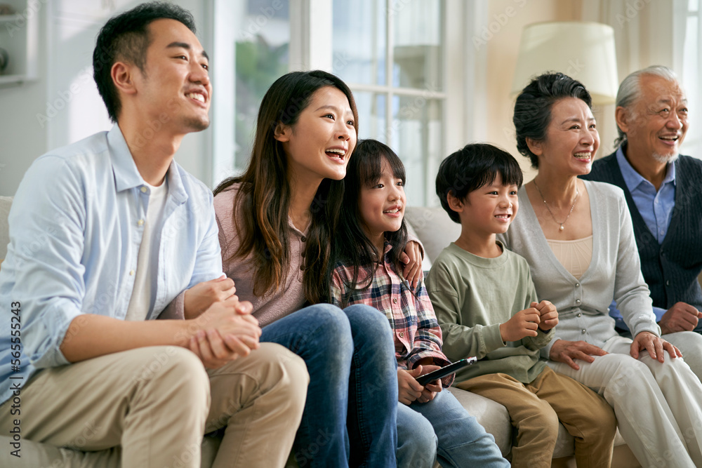 three generation asian family watching tv together at home three generation asian family watching tv together at home