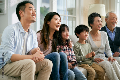 three generation asian family watching tv together at home