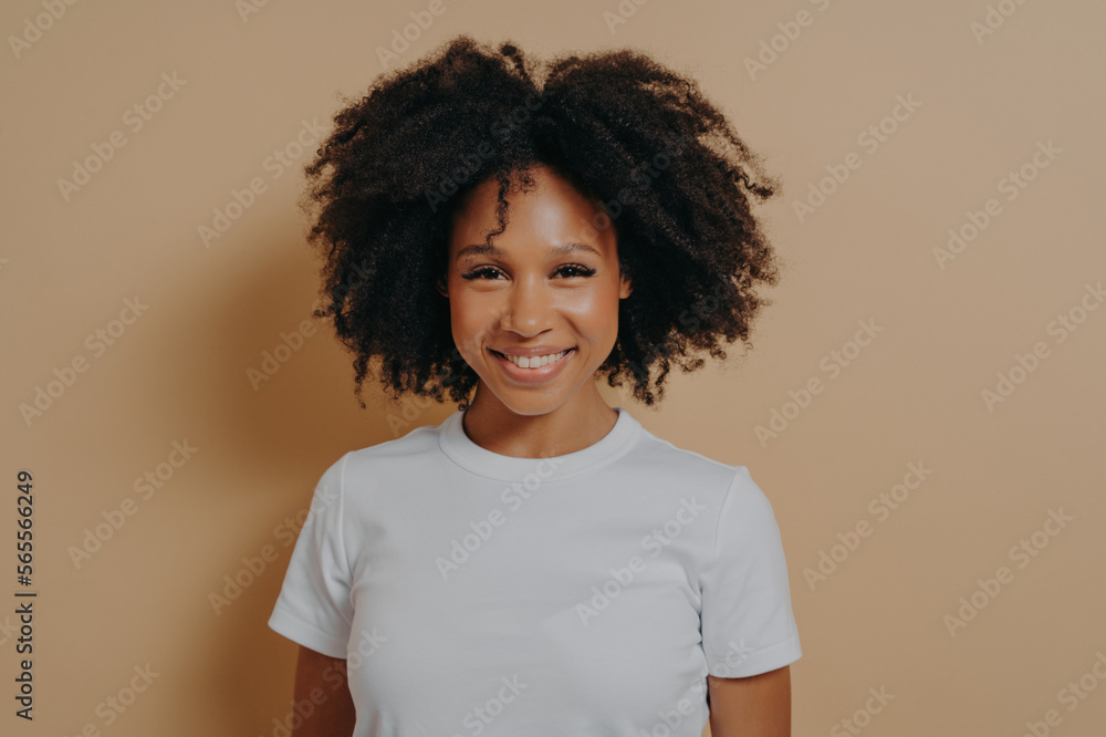 Portrait of cheerful dark skinned woman expressing happiness while standing on beige background